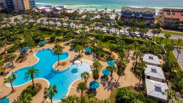 Un resort con una piscina grande, palmeras y vistas al océano.