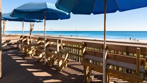 Una terraza de madera con bancos y sombrillas azules con vistas a la playa.
