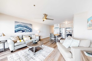 A modern living room with a grey sofa, a round coffee table, and a dining area with a table and chairs. - Beautiful Gulf Condo with Balcony, Outdoor Shower & Shared Pool (Destin)