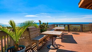 Een houten terras met buitenmeubels, een palmboom en uitzicht op de oceaan.