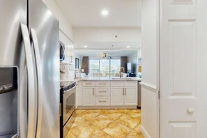 A modern kitchen with white cabinets, a stainless steel refrigerator, and a large window providing a view of the outside. - Amazing High Pointe condo with grill, hot tub, pool, tennis & pickleball (Seacrest)