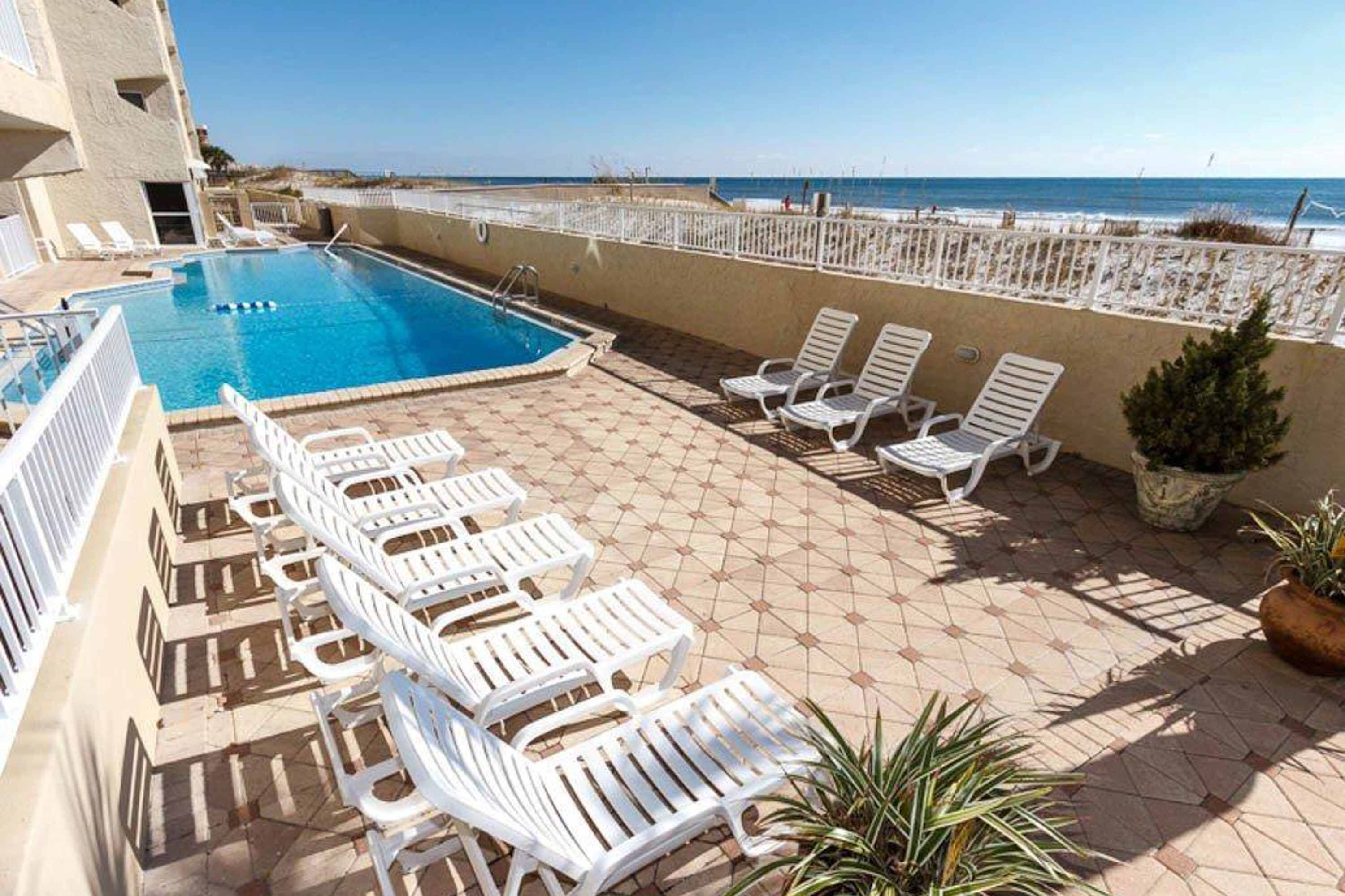 A pool area with white lounge chairs and a view of the beach.