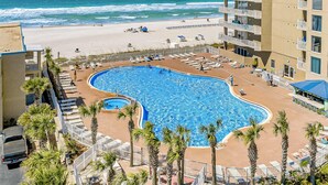 Ein Hotel mit großem Pool, umgeben von Liegestühlen und Palmen, mit Blick auf einen Strand und den Ozean.