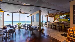 Ein Restaurant mit Meerblick, ausgestattet mit Tischen, Stühlen, einer Bar und Deckenventilatoren.