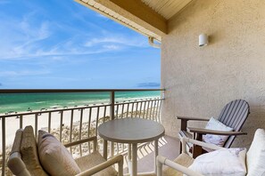 A balcony with a view of the beach, a round table, and two chairs. - Charming Condo with Gulf View! Grill, Pools, Beach Access (Destin)