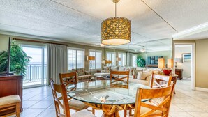 A spacious living room with a glass-top dining table surrounded by wooden chairs, a large chandelier, and a view of the outdoors through large windows. - 6th-floor, updated condo with beach service - near dining (Fort Walton Beach)
