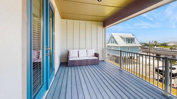 Un balcon doté d’un plancher en bois bleu, d’un mur blanc et d’une porte bleue avec des panneaux de verre.
