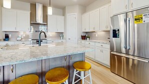 Une cuisine moderne avec des meubles blancs, un réfrigérateur en acier inoxydable, un îlot en marbre avec des tabourets et des luminaires suspendus.