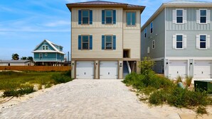 Une propriété située en bord de mer, avec un chemin pavé menant à un immeuble à plusieurs étages doté de deux garages.