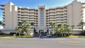 Ein mehrstöckiges Hotel mit einem zentralen Eingang, umgeben von Palmen und einem gepflegten Rasen.