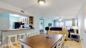 A spacious living area with a dining table, white chairs, a sofa, and a kitchen area with cabinets and a microwave. - Updated, first-floor, open, airy condo with great views - close to dining (Fort Walton Beach)