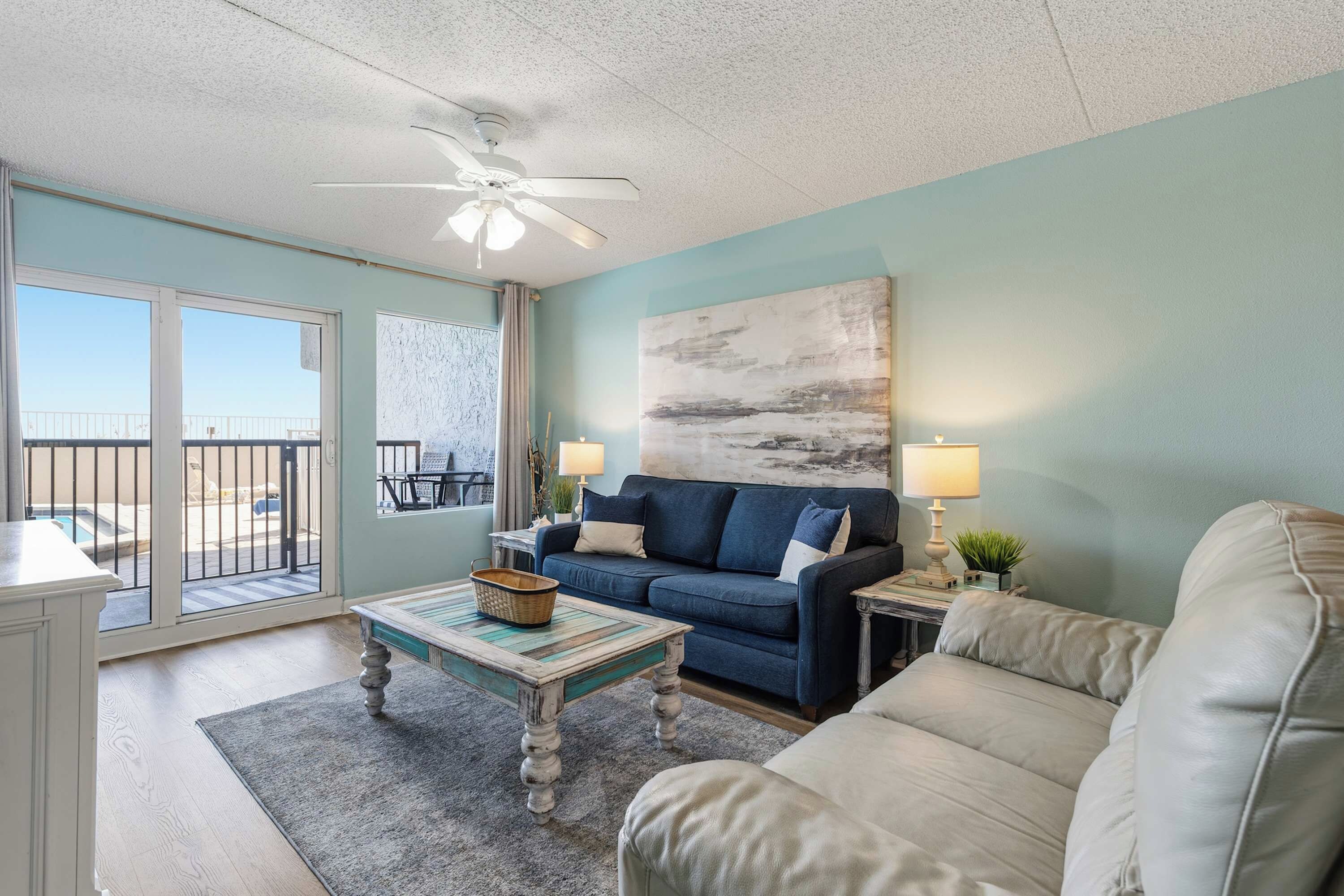 A living room with a blue sofa, a white armchair, a coffee table, and a ceiling fan.