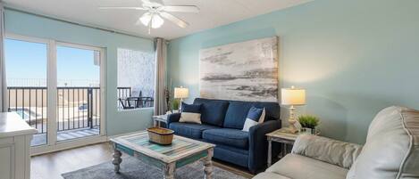 A living room with a blue sofa, a white armchair, a coffee table, and a ceiling fan.
