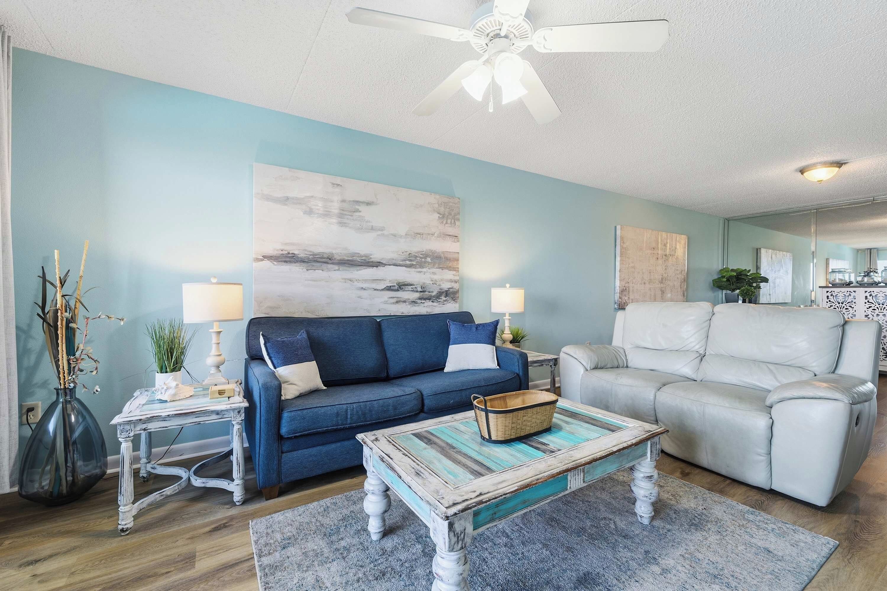 Un salon avec un canapé bleu, un fauteuil blanc, une table basse et un ventilateur de plafond.