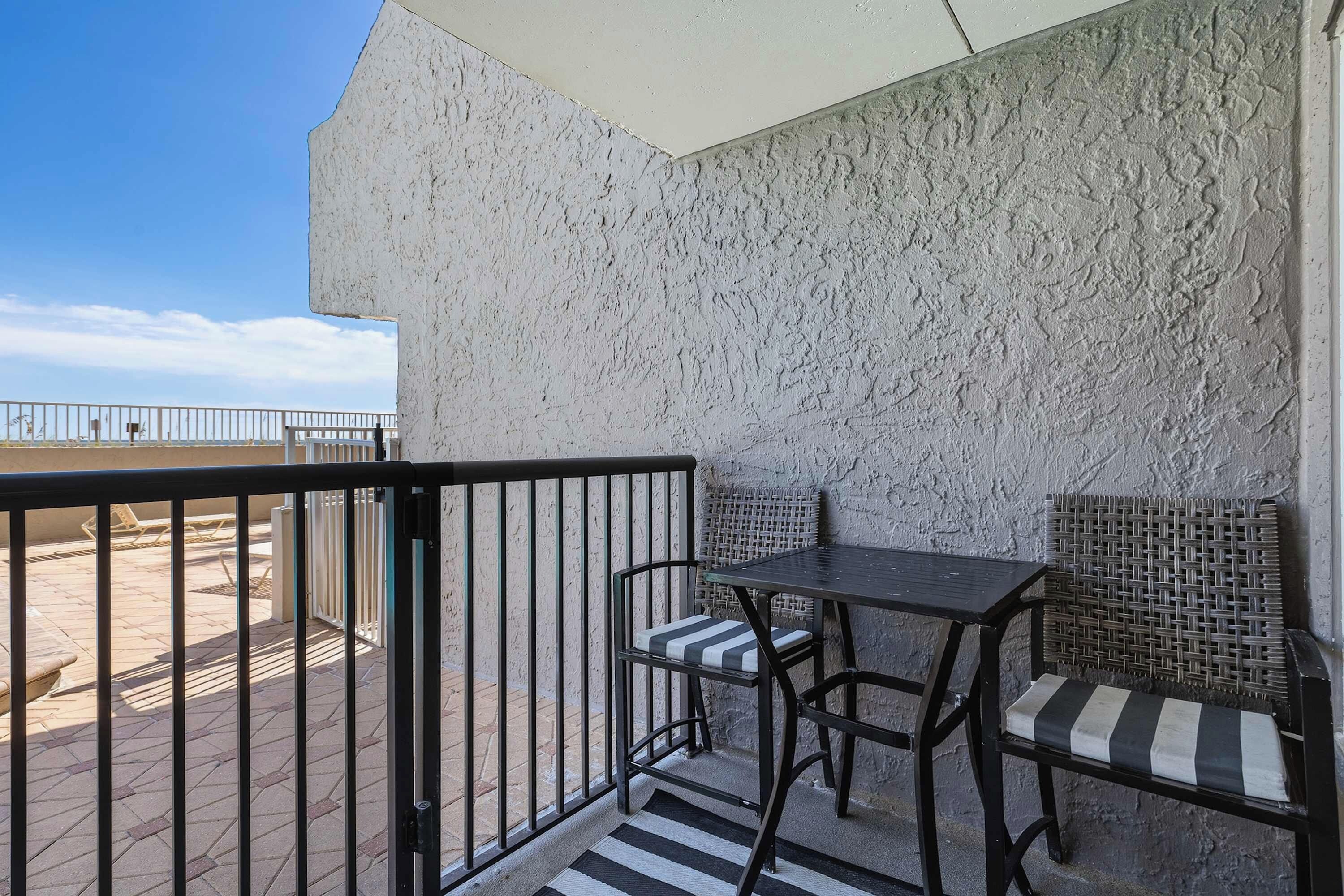 Ein Balkon mit Tisch und Stühlen, Blick auf den Strand und eine strukturierte Wand.