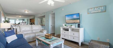 A living room with a ceiling fan, a television on a white dresser, and a 'BEACH' sign on the wall.