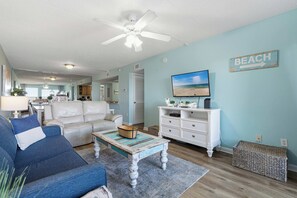 Ein Wohnzimmer mit Deckenventilator, einem Fernseher auf einer weißen Kommode und einem Schild mit der Aufschrift 'BEACH'.