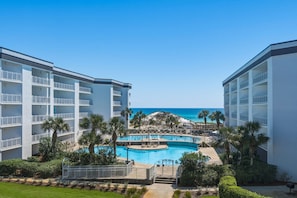 A resort with a central pool, palm trees, and a view of the ocean. - Charming two-bedroom with bunks, balcony overlooking pool & pickleball (Santa Rosa Beach)