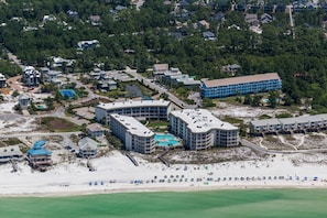 Vista aérea de um resort à beira-mar com vários edifícios, uma praia e um complexo de piscinas.
