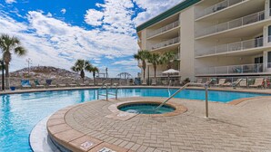 Una piscina con jacuzzi, palmeras y un edificio con balcones.