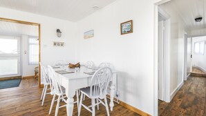 Un espace repas avec une table et des chaises blanches, un plancher en bois et des murs blancs.
