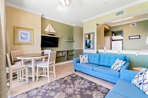 Un salon avec un canapé bleu, une table à manger avec des chaises, un téléviseur et une bibliothèque.