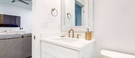 A modern bathroom with a white vanity, a large mirror, a toilet, and a ceiling fan.