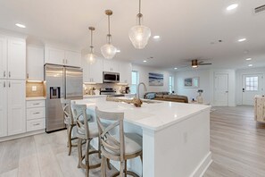 A modern kitchen with white cabinetry, a large island with bar stools, stainless steel appliances, and pendant lighting. - Dog-friendly house near the beach, balconies, washer&dryer, & cable (Navarre)