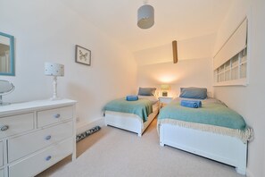 A bedroom with two beds, a dresser, a mirror, and a bedside table with a lamp. - The Old Post Office - sleeps 6 guests  in 3 bedrooms (Sedgeford)