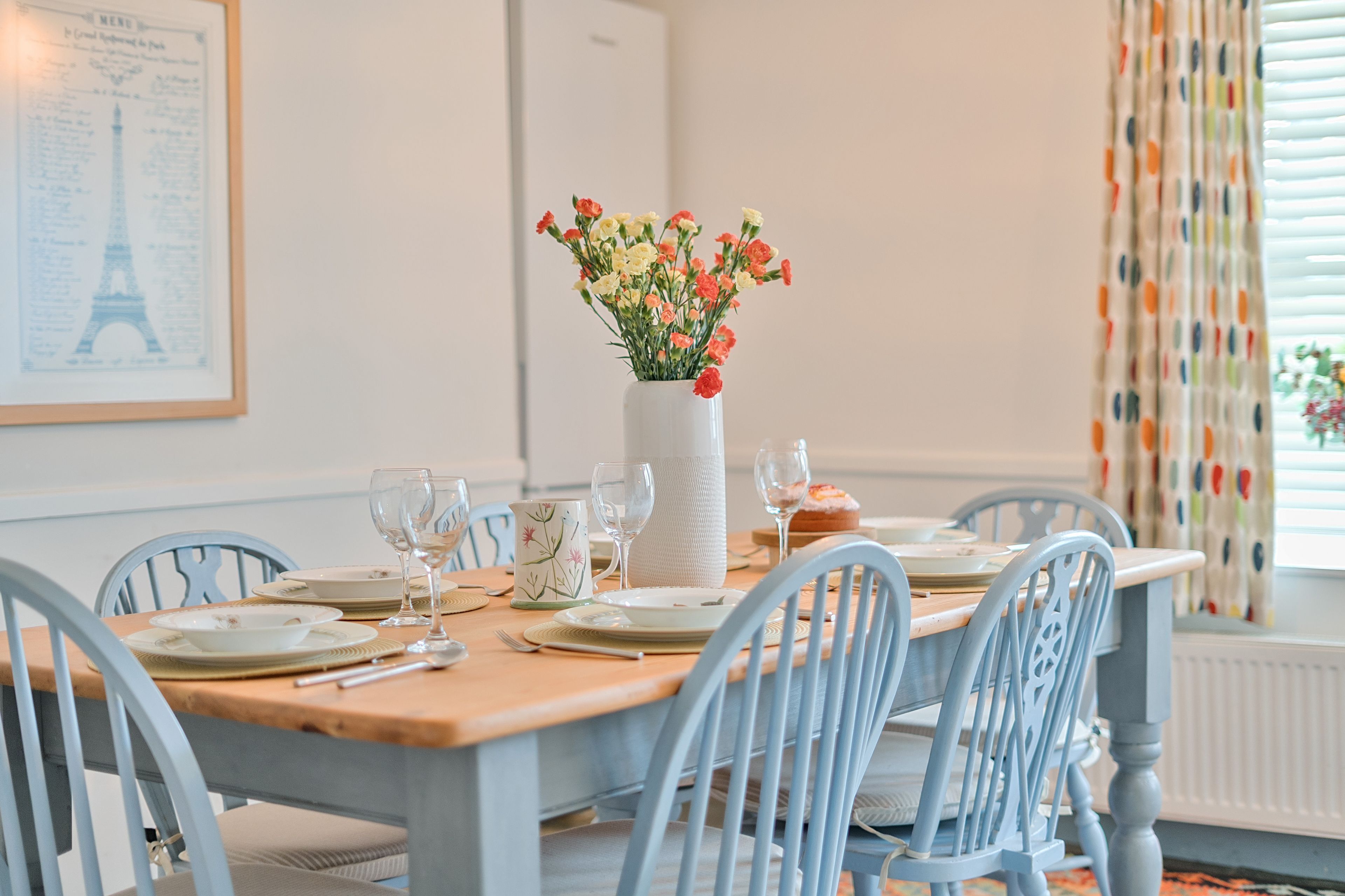 A dining table set with plates, glasses, and a vase of flowers.