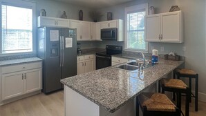 Una cocina moderna con armarios blancos, encimeras de granito, electrodomésticos de acero inoxidable y una isla grande con taburetes de bar.