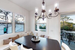A dining area with a dark wooden table, white chairs, and a chandelier. There are large windows with views of trees and a building. - Home near beach and 30A with balcony, yard, patio, grill, Washer & Dryer (Santa Rosa Beach)
