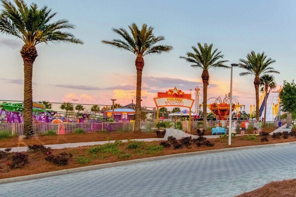 Une allée pavée bordée de palmiers et un panneau indiquant « Parc d’attractions ».