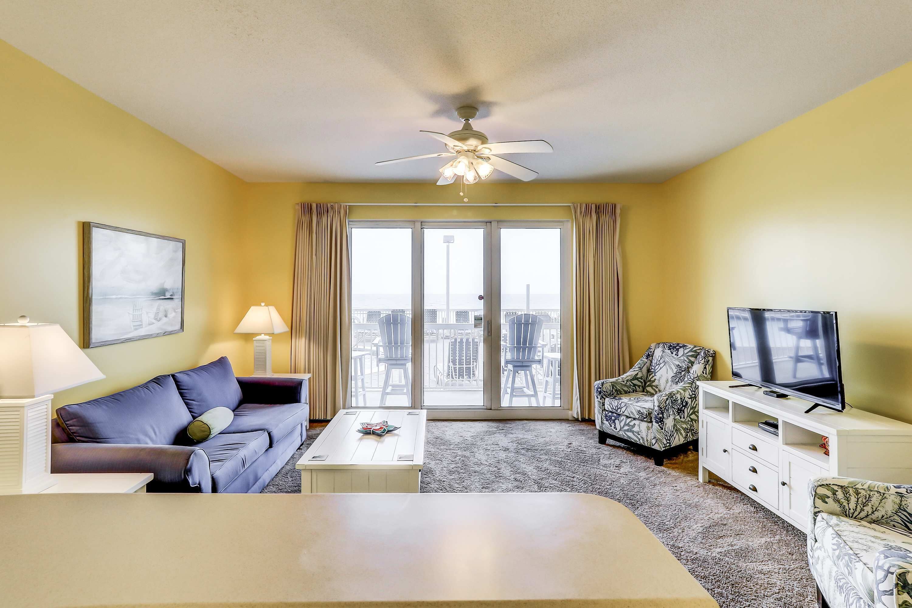 A living room with a sofa, coffee table, TV stand, and a ceiling fan.