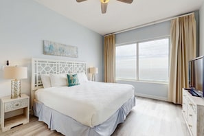 A spacious bedroom with a large bed, a ceiling fan, a television, and a window with curtains. - Beautiful and spacious condo with shared pool & beach access (Miramar Beach)