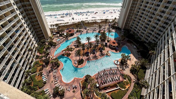 A high-rise hotel with a rooftop pool area, including multiple swimming pools and lounge areas, overlooking a beach. - Updated oceanfront condo with pools, hot tub, W/D, AC, & views (Panama City Beach)