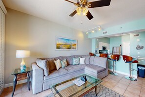 A living room with a sofa, a glass coffee table, a lamp, and a ceiling fan. - Updated oceanfront condo with pools, hot tub, W/D, AC, & views (Panama City Beach)