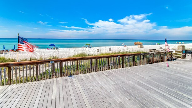 Eine Holzterrasse mit Blick auf einen Strand, bewacht von einer Flagge und mit Liegestühlen.