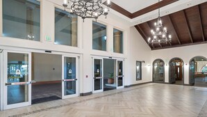 En rymlig entréhall med ett fiskbensmönstrat golv, stora glasdörrar med utrymningsskyltar och en kristallkrona.