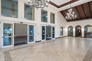 A spacious lobby with a herringbone floor pattern, large glass doors with exit signs, and a chandelier. - Tasteful oceanfront condo with beach, pool, hot tub, & washer/dryer (Panama City Beach)