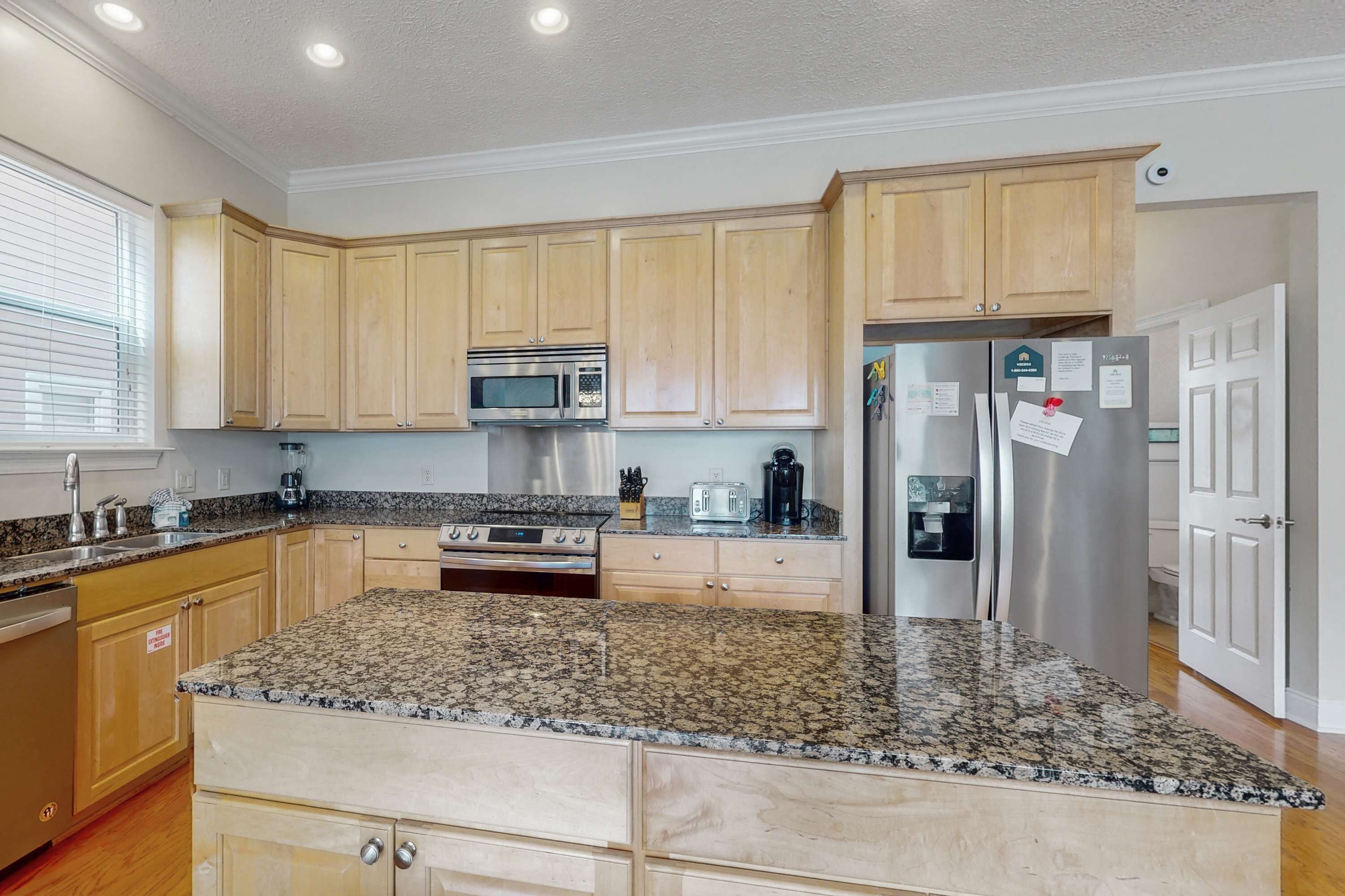A kitchen with granite countertops, wooden cabinets, a stainless steel refrigerator, and a built-in oven.