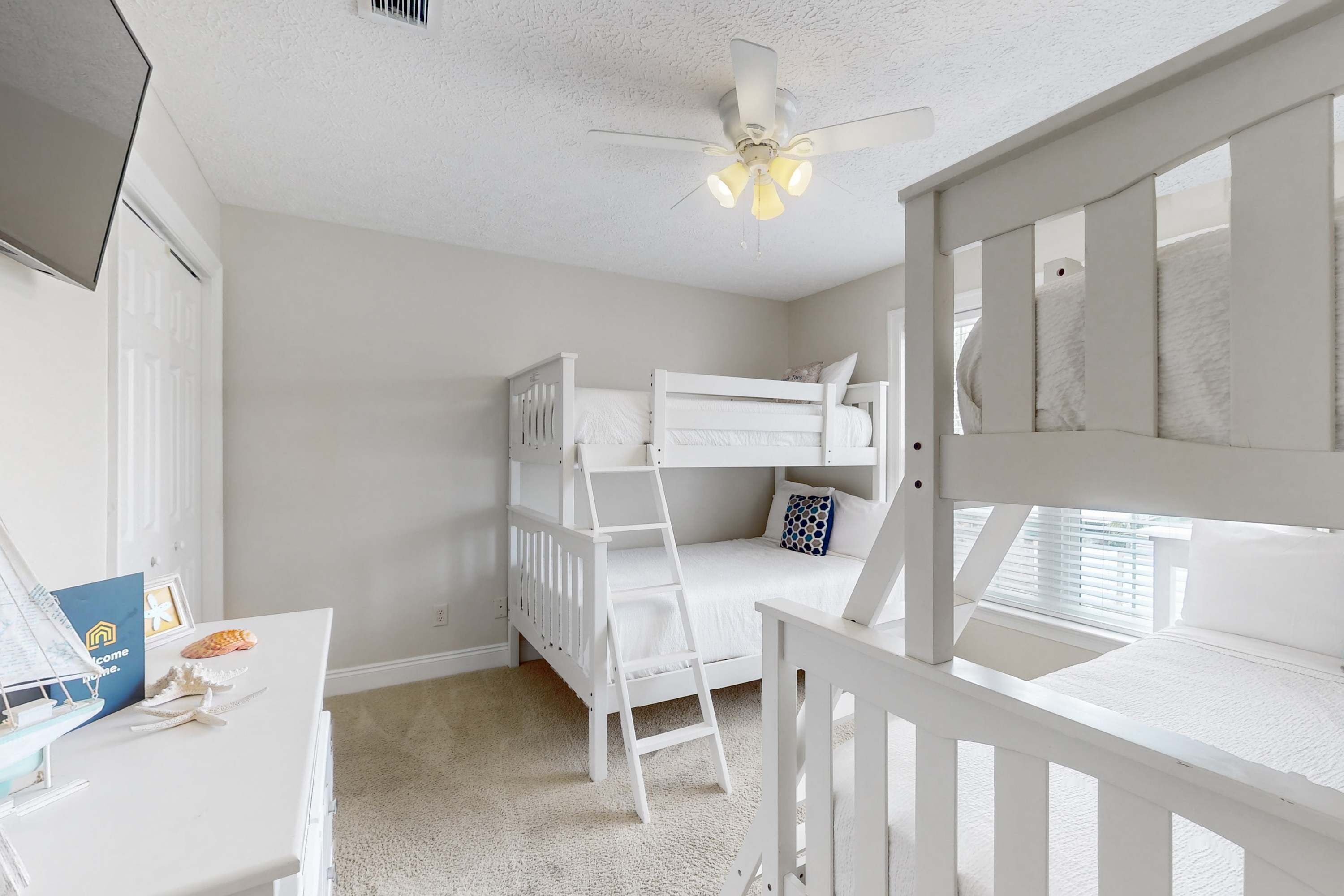 A child's bedroom with bunk beds, a desk, and a ceiling fan.