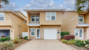 A two-story residential building with a garage, a covered driveway, and a well-maintained garden with various plants. - Ideal Coastal Retreat w/ Shared Pool, Private Balcony, & Beach Access Nearby (Panama City Beach)