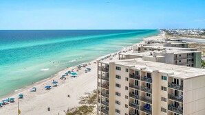 A beachfront hotel with multiple balconies, a sandy beach, and clear blue waters. - Gorgeous beachfront condo, shared pool and beach access (Panama City Beach)