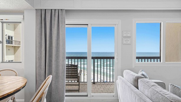 A room with a balcony overlooking the ocean, a dining table, and a sofa. - Gorgeous beachfront condo, shared pool and beach access (Panama City Beach)