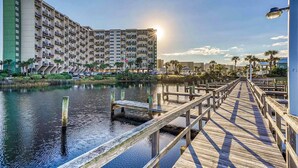 A waterfront hotel with a wooden pier, a large building with multiple balconies, and a calm water body. - Gorgeous beachfront condo, shared pool and beach access (Panama City Beach)