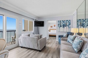 A room with a balcony, a sofa, a bed, and a TV. - Gorgeous beachfront condo, shared pool and beach access (Panama City Beach)
