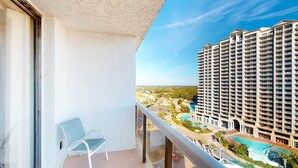 Un balcón con una silla, con vistas a un edificio alto que tiene piscina y zonas verdes.