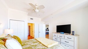 Een slaapkamer met een bed, een televisie, een dressoir en een plafondventilator.
