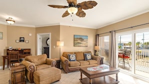 A living room with a ceiling fan, a sofa set, a coffee table, and a dining area with a view of the outdoors.
